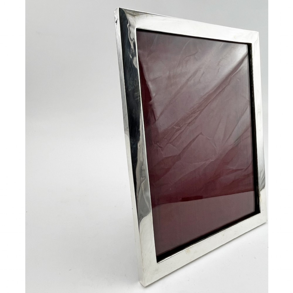 A rectangular sterling silver photo frame with a polished plain border standing vertically on an easel back. View III