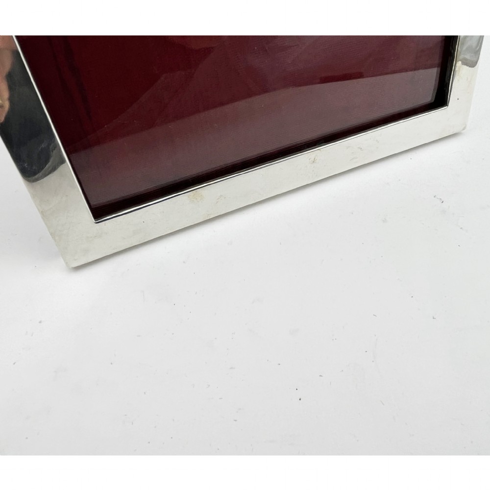 A rectangular sterling silver photo frame with a polished plain border standing vertically on an easel back. View IV