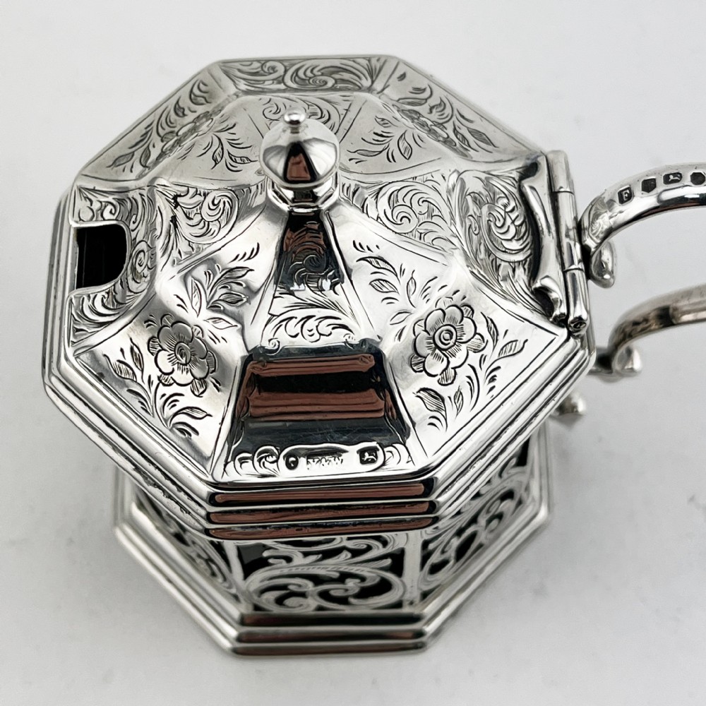 An octagonal Victorian sterling silver mustard pot featuring pierced foliate scrollwork, an engraved hinged lid with finial, a scroll handle, and an inner cobalt blue glass liner. View II
