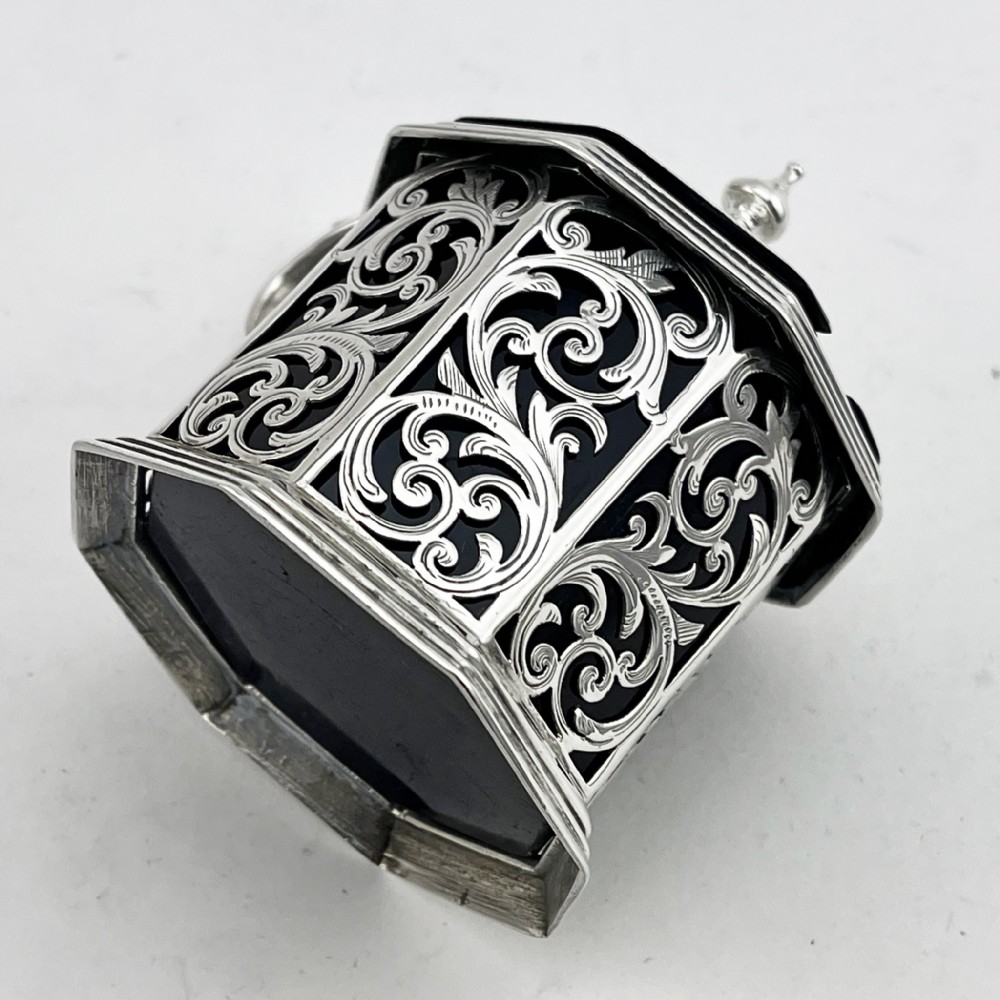 An octagonal Victorian sterling silver mustard pot featuring pierced foliate scrollwork, an engraved hinged lid with finial, a scroll handle, and an inner cobalt blue glass liner. View VI