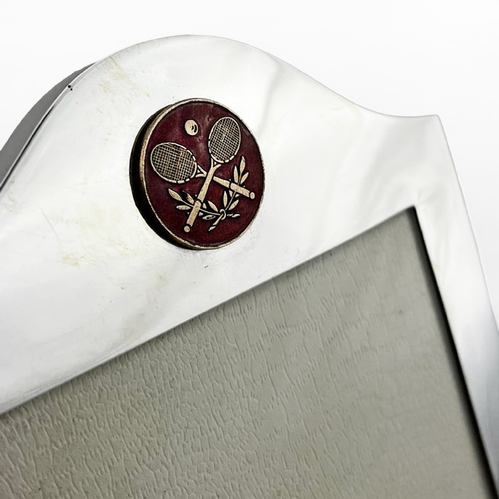 A sterling silver portrait photo frame featuring an arched top decorated with a round red enamel crest depicting crossed tennis racquets and a ball, supported by a rear easel stand. View II