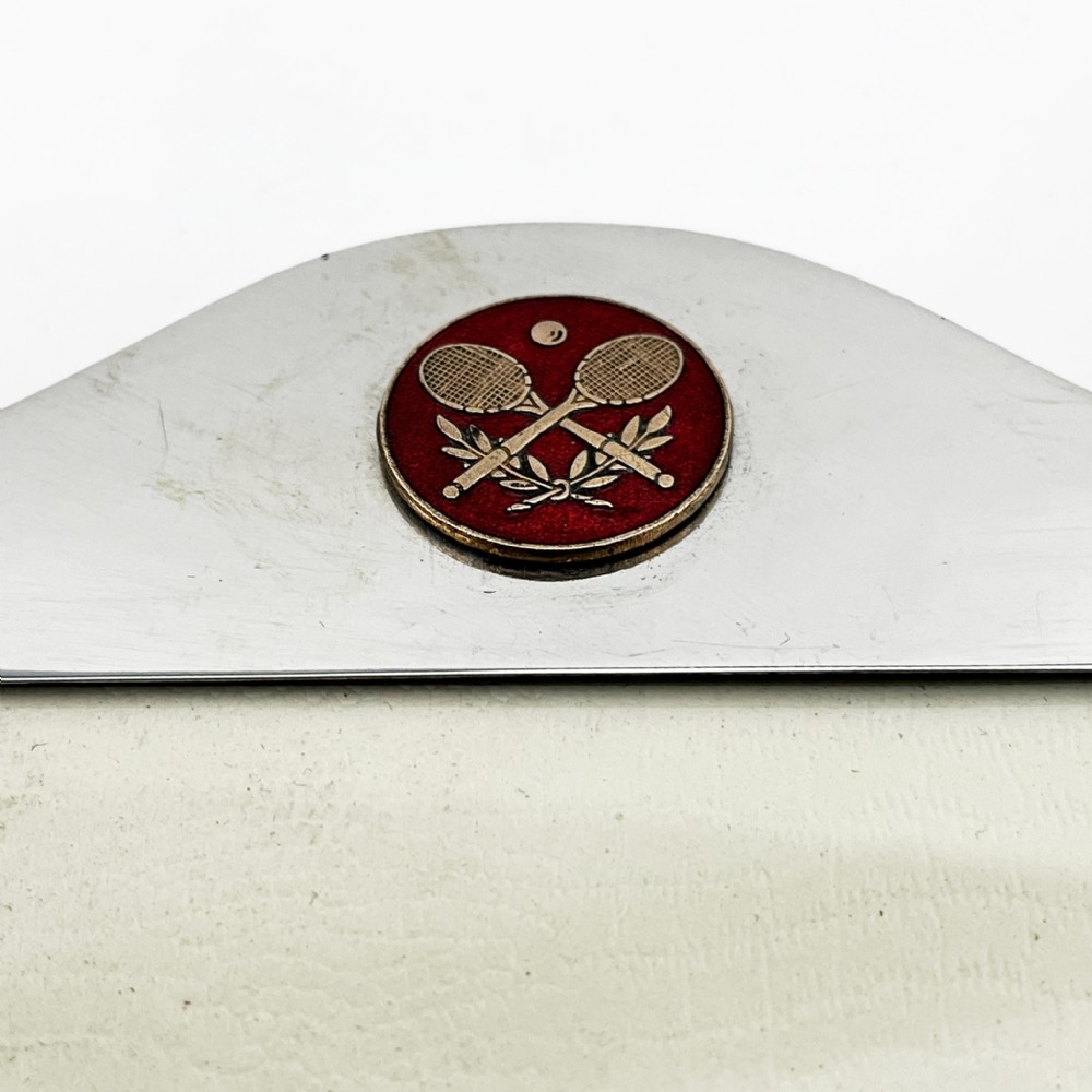A sterling silver portrait photo frame featuring an arched top decorated with a round red enamel crest depicting crossed tennis racquets and a ball, supported by a rear easel stand. View V