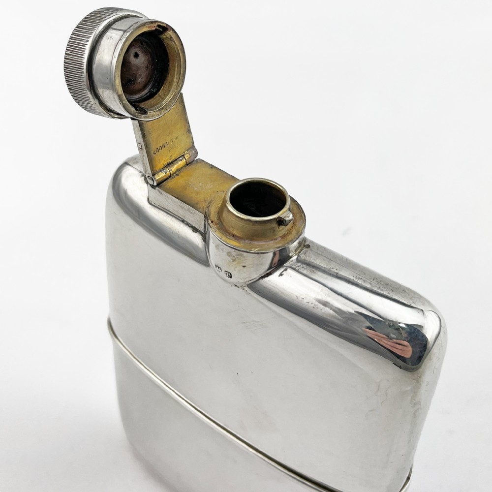A curved sterling silver hip flask with a hinged screw cap and hallmarks stamped along the side. View II