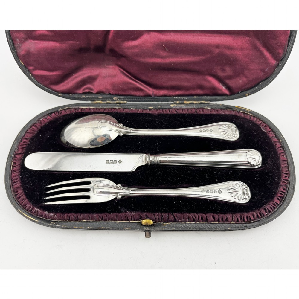 A three-piece Victorian sterling silver christening set featuring a spoon, knife, and fork arranged inside an open black leatherette presentation box lined with plum silk and velvet. View II