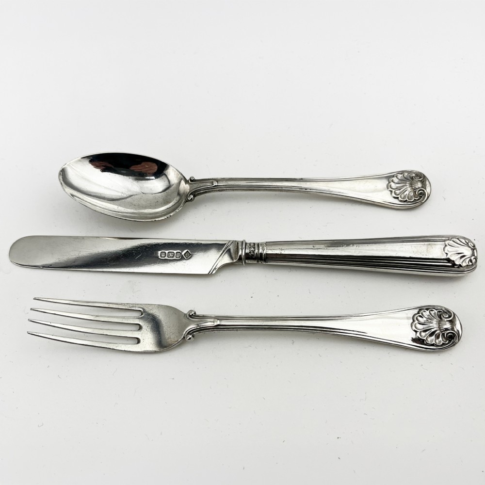 A three-piece Victorian sterling silver christening set featuring a spoon, knife, and fork arranged inside an open black leatherette presentation box lined with plum silk and velvet. View IV