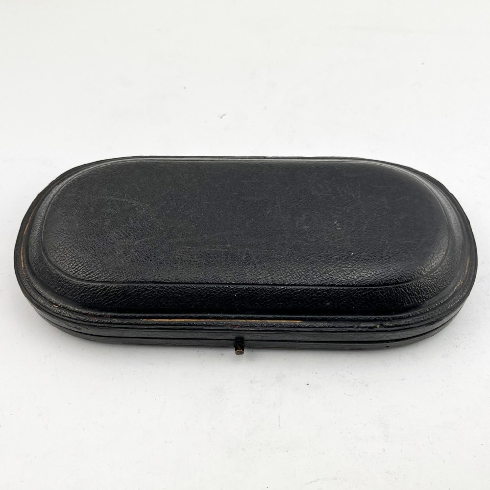 A three-piece Victorian sterling silver christening set featuring a spoon, knife, and fork arranged inside an open black leatherette presentation box lined with plum silk and velvet. View VI