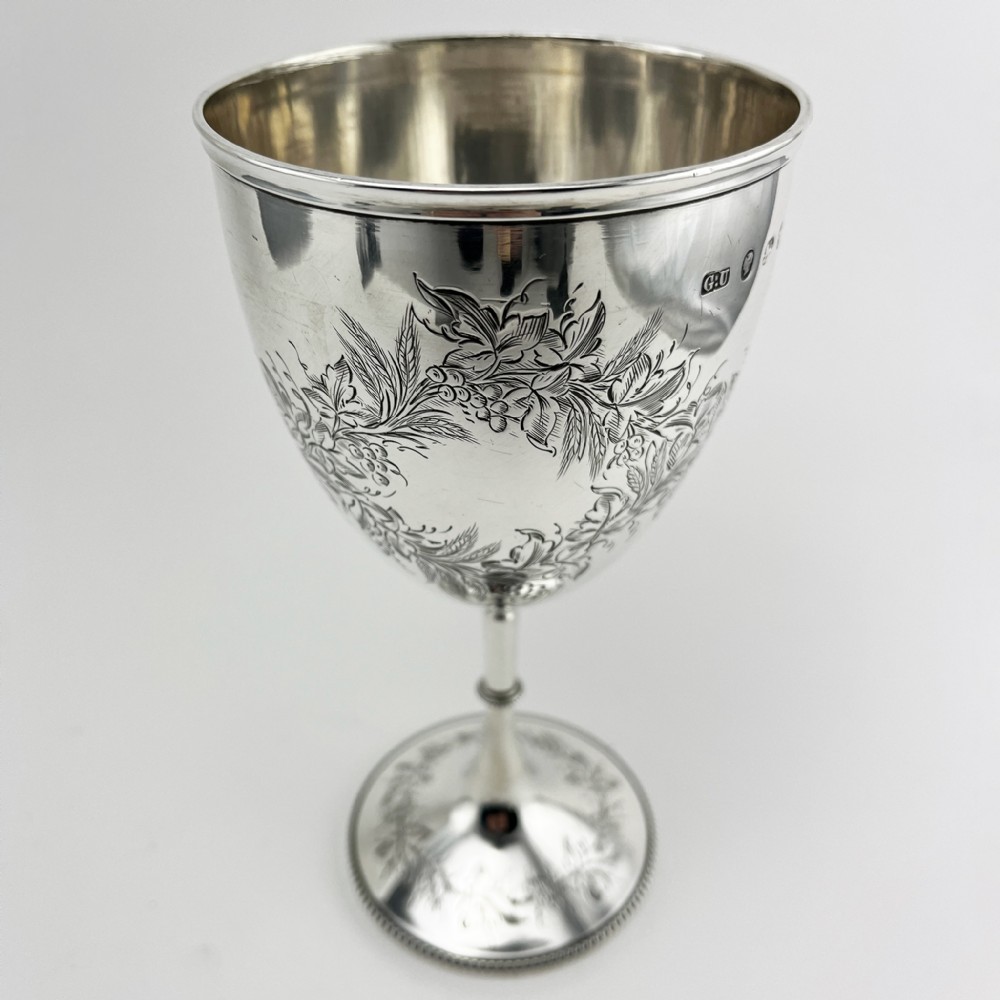 A Victorian sterling silver goblet featuring detailed floral foliage engraving around the bowl, a central knopped stem, and an engraved circular base.