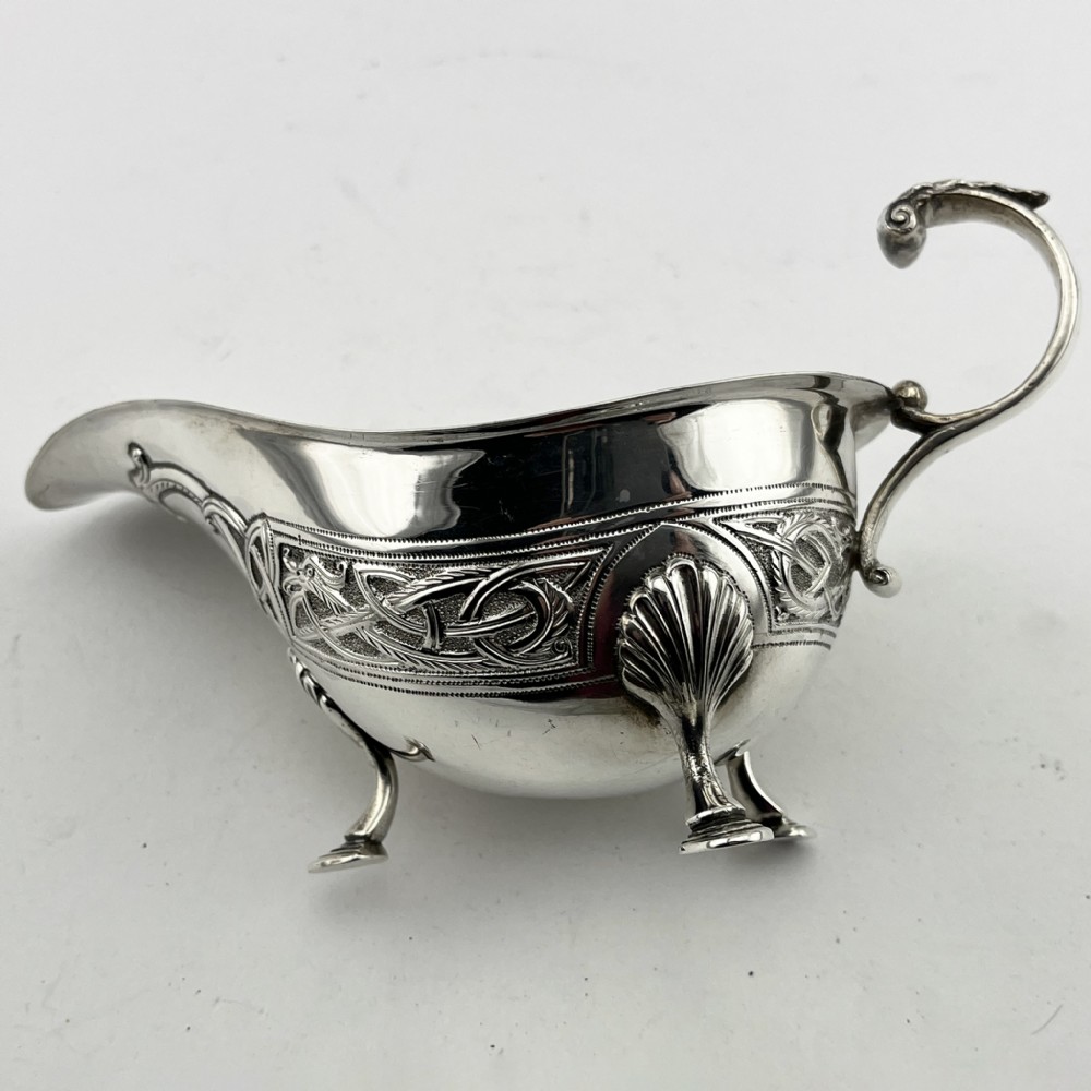 An Irish sterling silver sauce boat decorated with chased Celtic knotwork, featuring a scroll handle and three hoof feet. View II