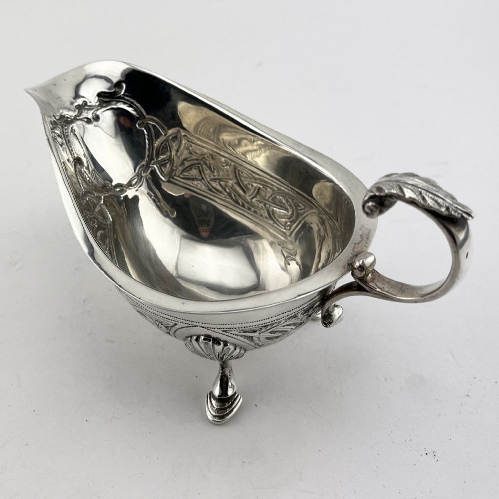 An Irish sterling silver sauce boat decorated with chased Celtic knotwork, featuring a scroll handle and three hoof feet. View III