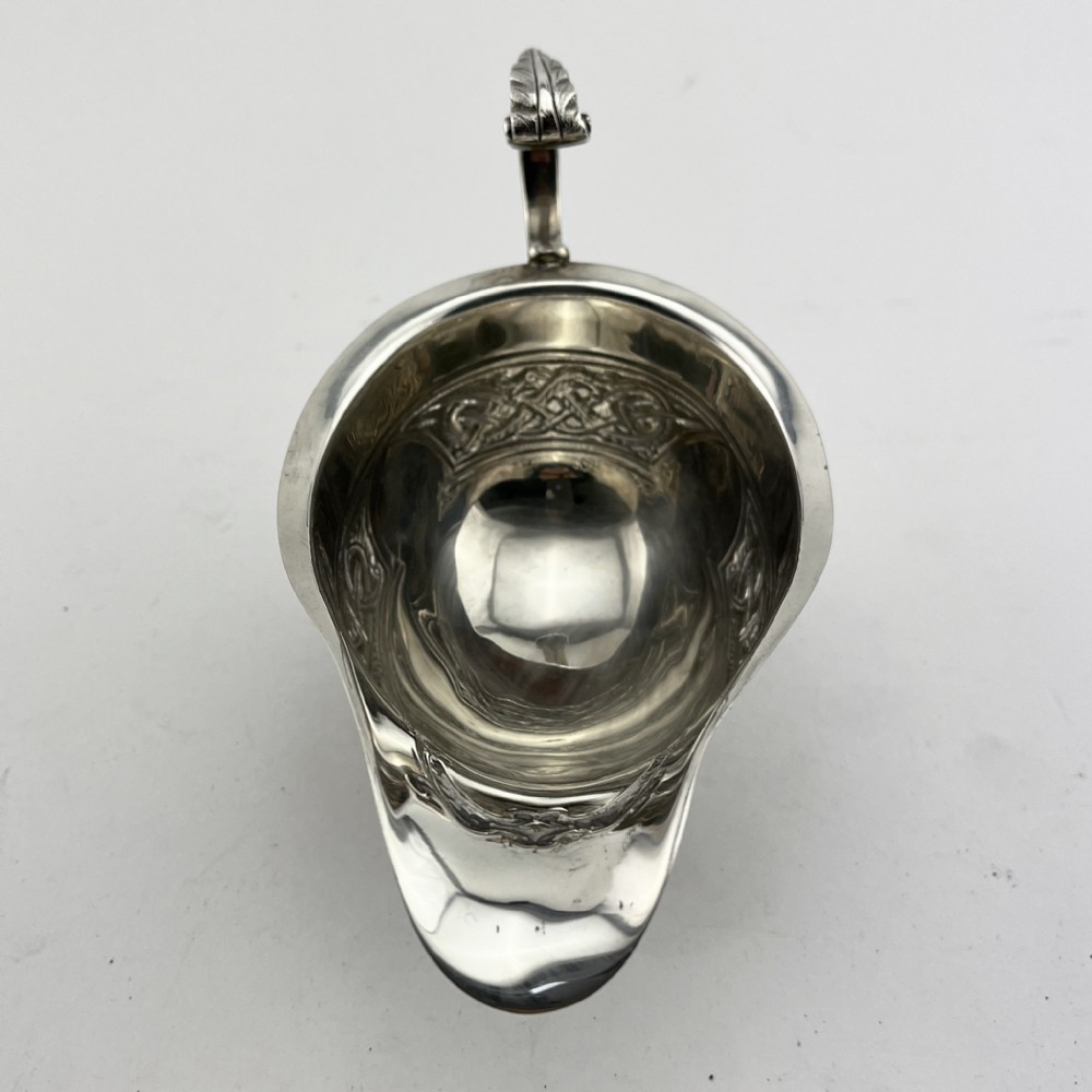 An Irish sterling silver sauce boat decorated with chased Celtic knotwork, featuring a scroll handle and three hoof feet. View IV
