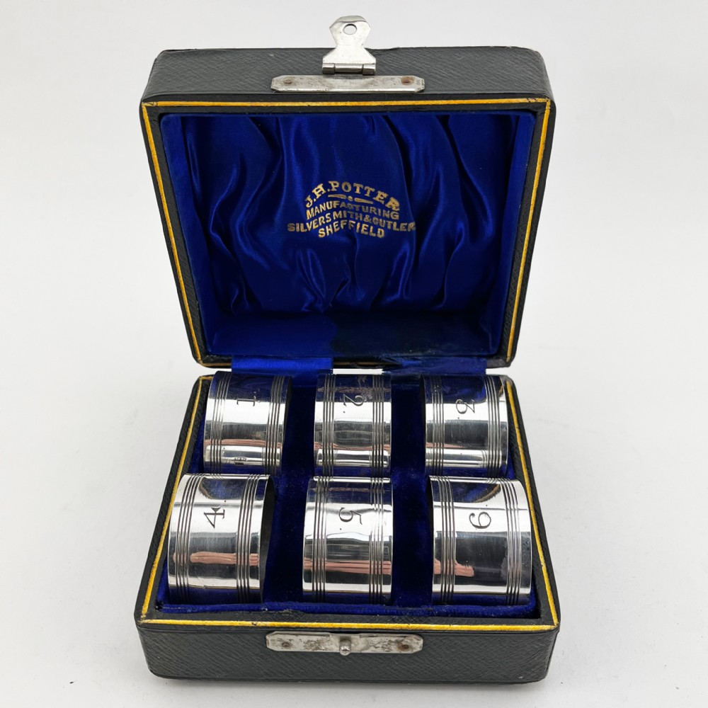 A set of six silver-plated napkin rings numbered one to six with reeded borders, stored in an open black case lined with blue silk and velvet.