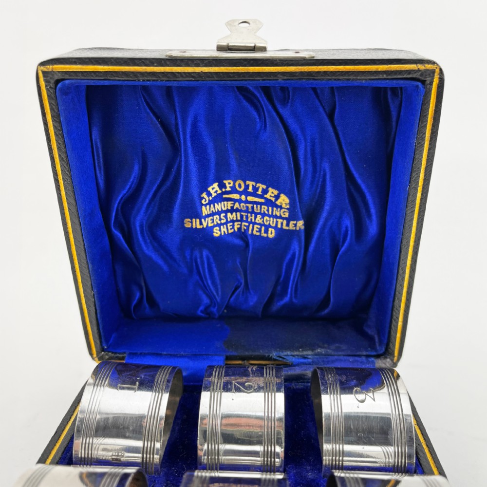 A set of six silver-plated napkin rings numbered one to six with reeded borders, stored in an open black case lined with blue silk and velvet. View III