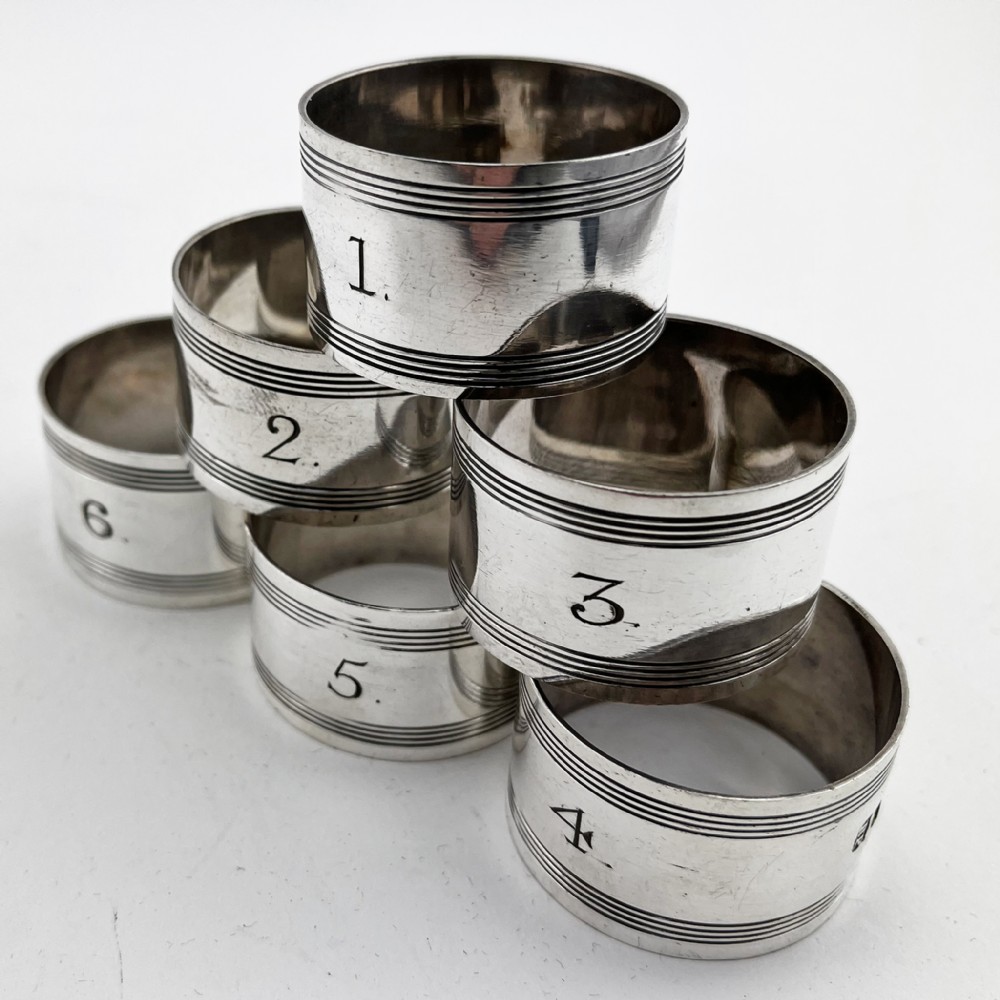 A set of six silver-plated napkin rings numbered one to six with reeded borders, stored in an open black case lined with blue silk and velvet. View IV