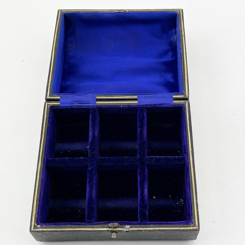 A black fitted presentation box open to display six plain sterling silver napkin rings numbered one through six on cobalt blue velvet lining. View IV