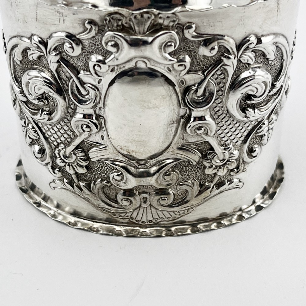 An oval Victorian sterling silver tea caddy featuring chased scrollwork decoration, a blank central cartouche, a scalloped border, and a pull-off cap lid. View II
