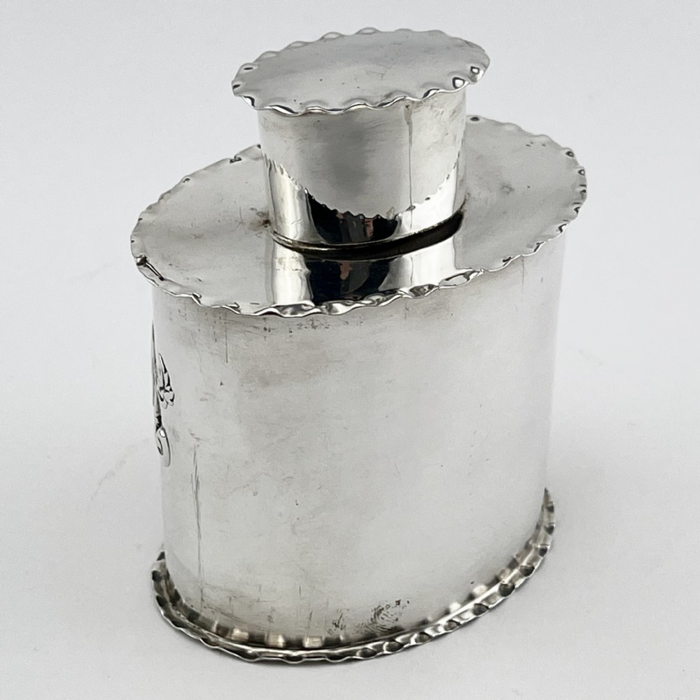 An oval Victorian sterling silver tea caddy featuring chased scrollwork decoration, a blank central cartouche, a scalloped border, and a pull-off cap lid. View III