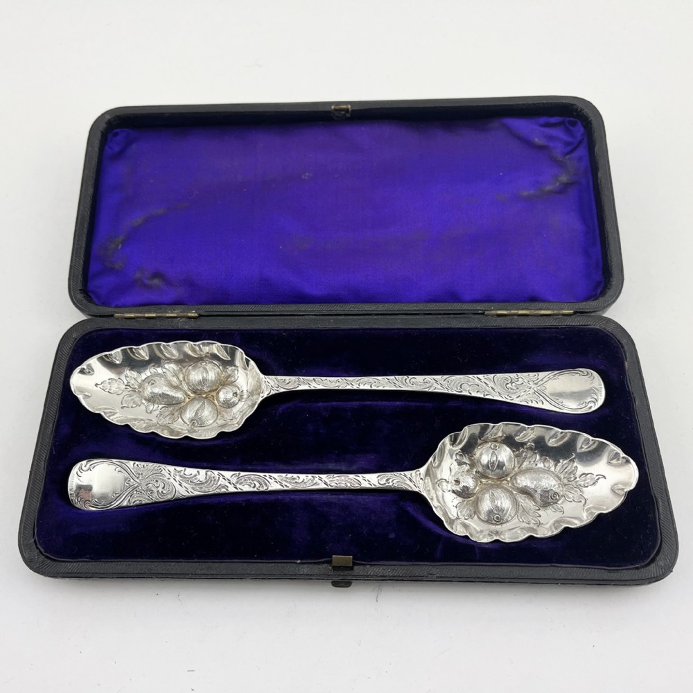 A pair of George III sterling silver berry spoons with fruit embossed bowls and chased handles, presented in a black velvet and purple silk lined case.