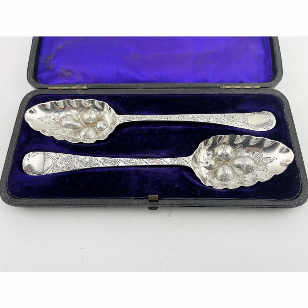 A pair of George III sterling silver berry spoons with fruit embossed bowls and chased handles, presented in a black velvet and purple silk lined case. View II