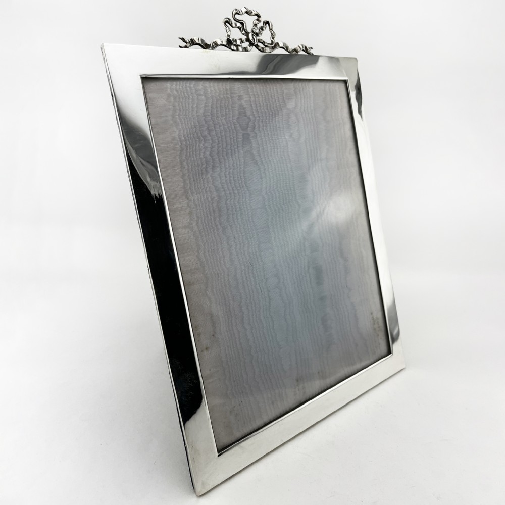 A rectangular sterling silver photo frame featuring a plain polished border topped with a bow ribbon motif.