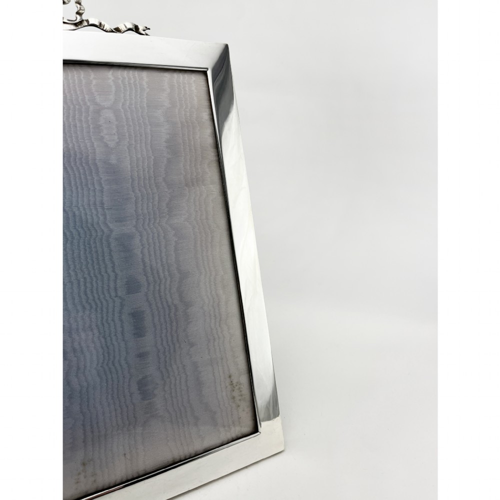 A rectangular sterling silver photo frame featuring a plain polished border topped with a bow ribbon motif. View II