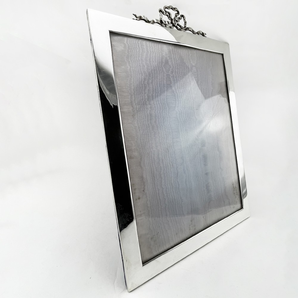 A rectangular sterling silver photo frame featuring a plain polished border topped with a bow ribbon motif. View III