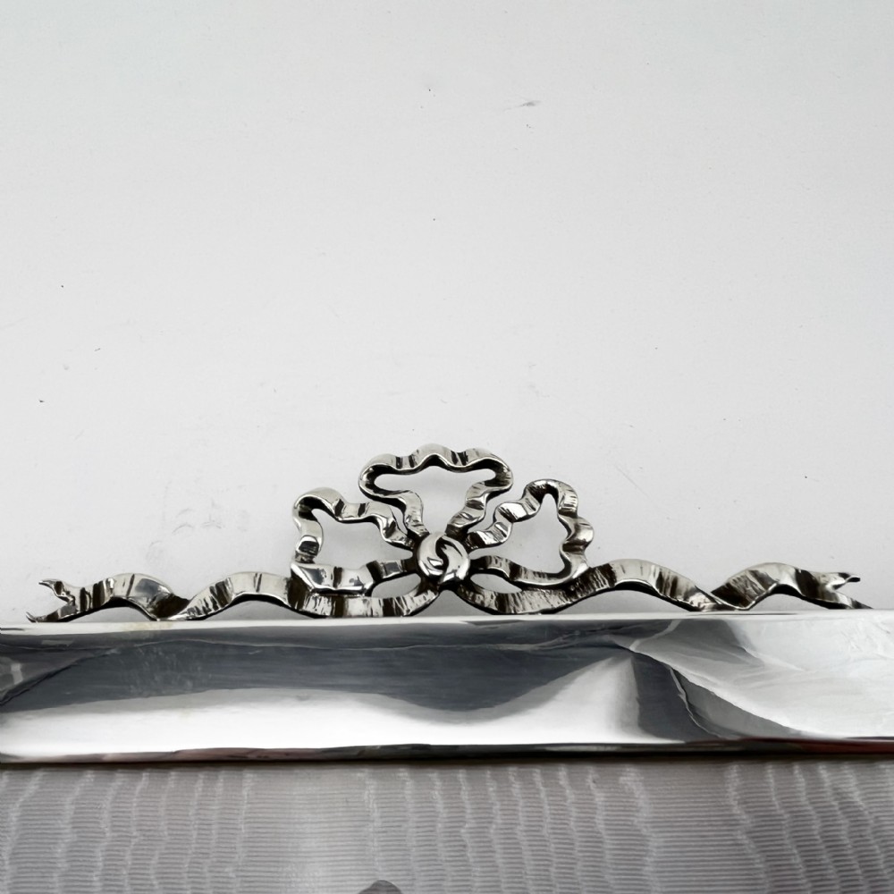 A rectangular sterling silver photo frame featuring a plain polished border topped with a bow ribbon motif. View IV