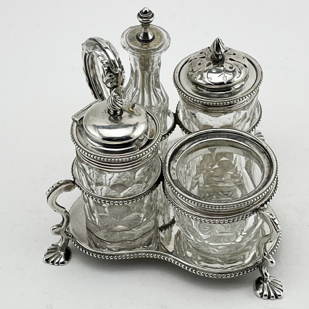 A Victorian sterling silver cruet stand holding four cut glass vessels with silver mounts, featuring shell feet and a central handle.