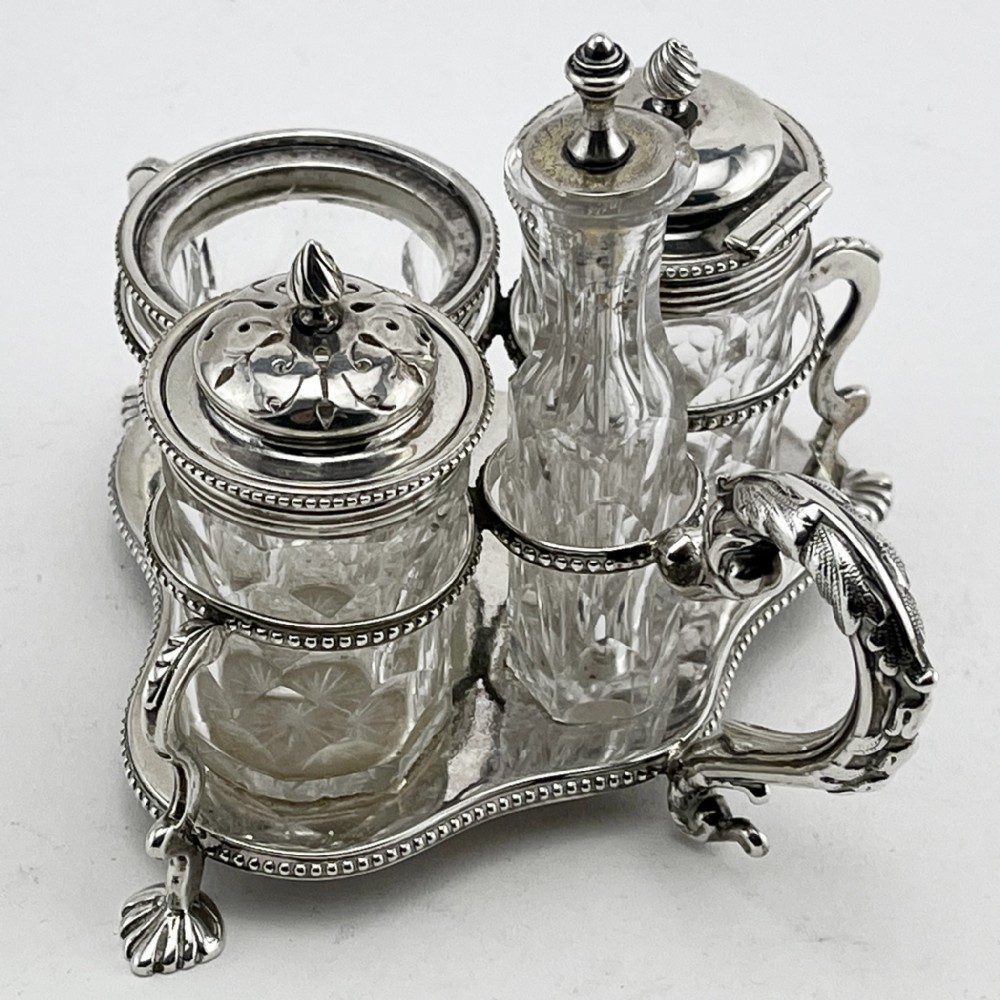 A Victorian sterling silver cruet stand holding four cut glass vessels with silver mounts, featuring shell feet and a central handle. View II