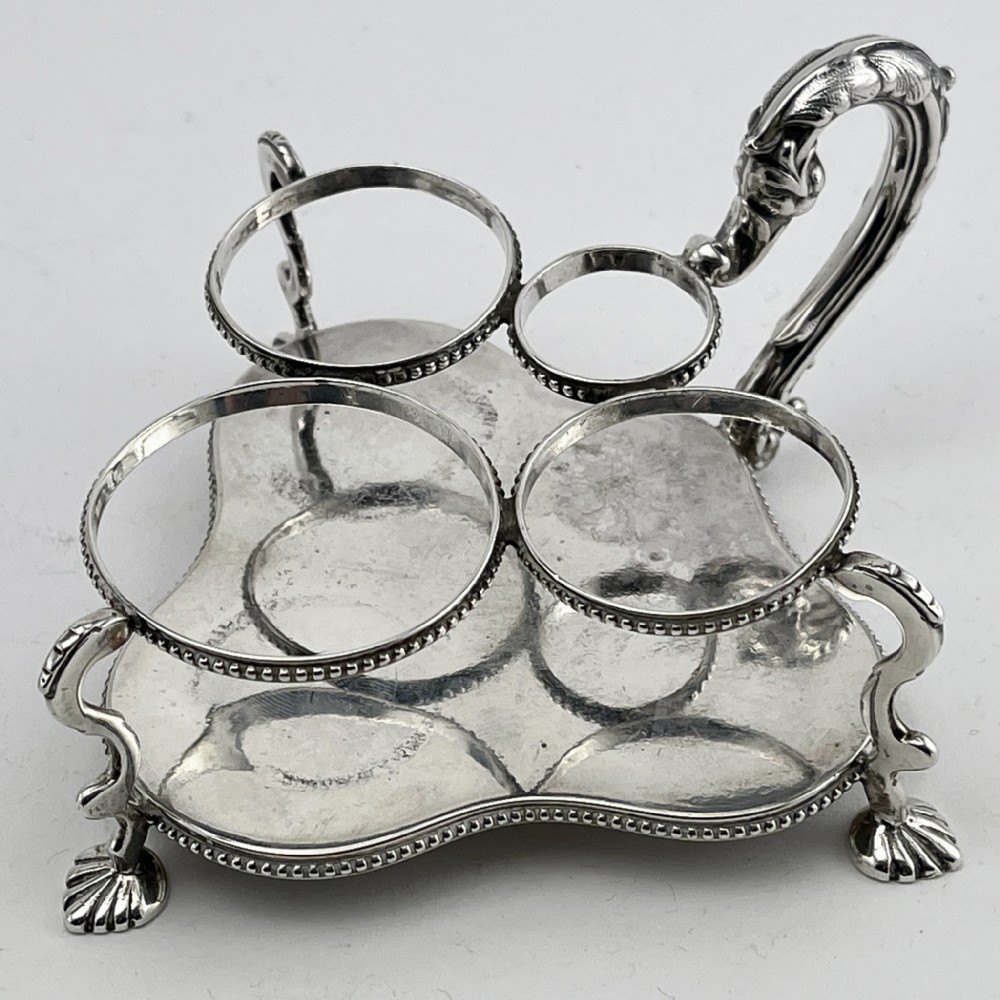 A Victorian sterling silver cruet stand holding four cut glass vessels with silver mounts, featuring shell feet and a central handle. View III