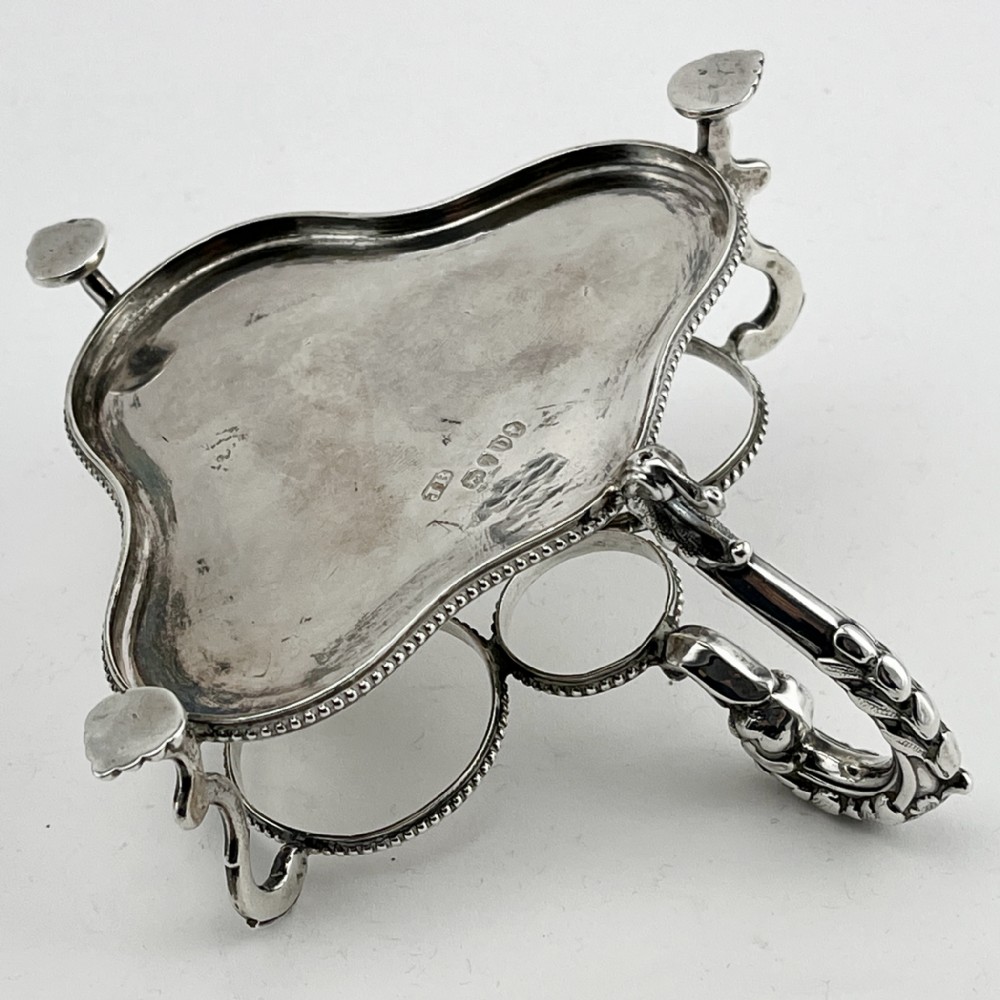 A Victorian sterling silver cruet stand holding four cut glass vessels with silver mounts, featuring shell feet and a central handle. View IV