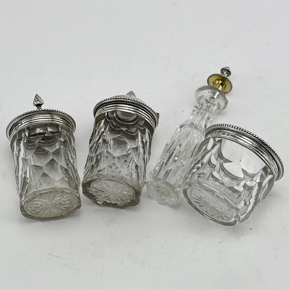 A Victorian sterling silver cruet stand holding four cut glass vessels with silver mounts, featuring shell feet and a central handle. View V