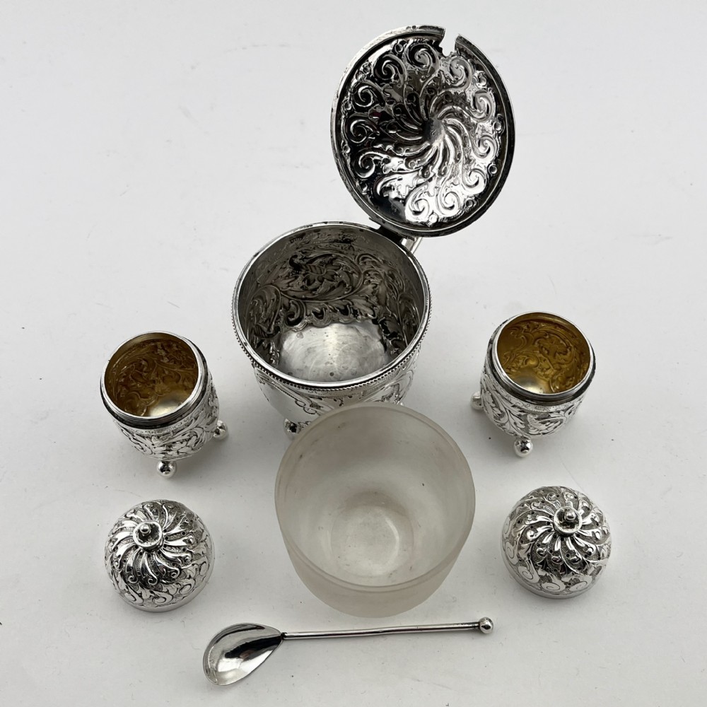 A Victorian sterling silver three-piece condiment set with floral repousse engraving housed inside an open velvet-lined presentation case. View III