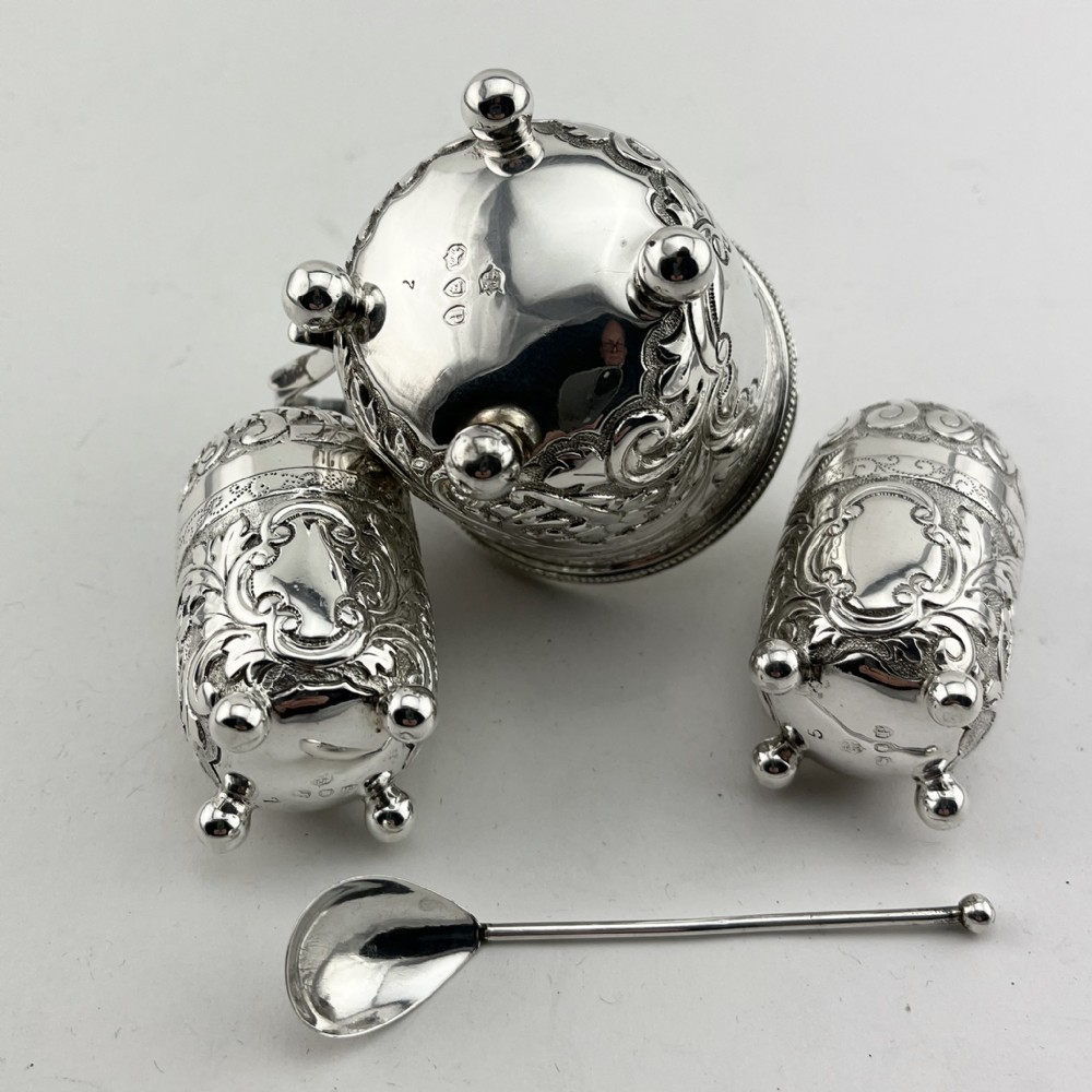 A Victorian sterling silver three-piece condiment set with floral repousse engraving housed inside an open velvet-lined presentation case. View V