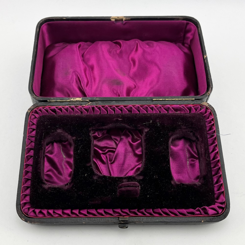 A Victorian sterling silver three-piece condiment set with floral repousse engraving housed inside an open velvet-lined presentation case. View VII