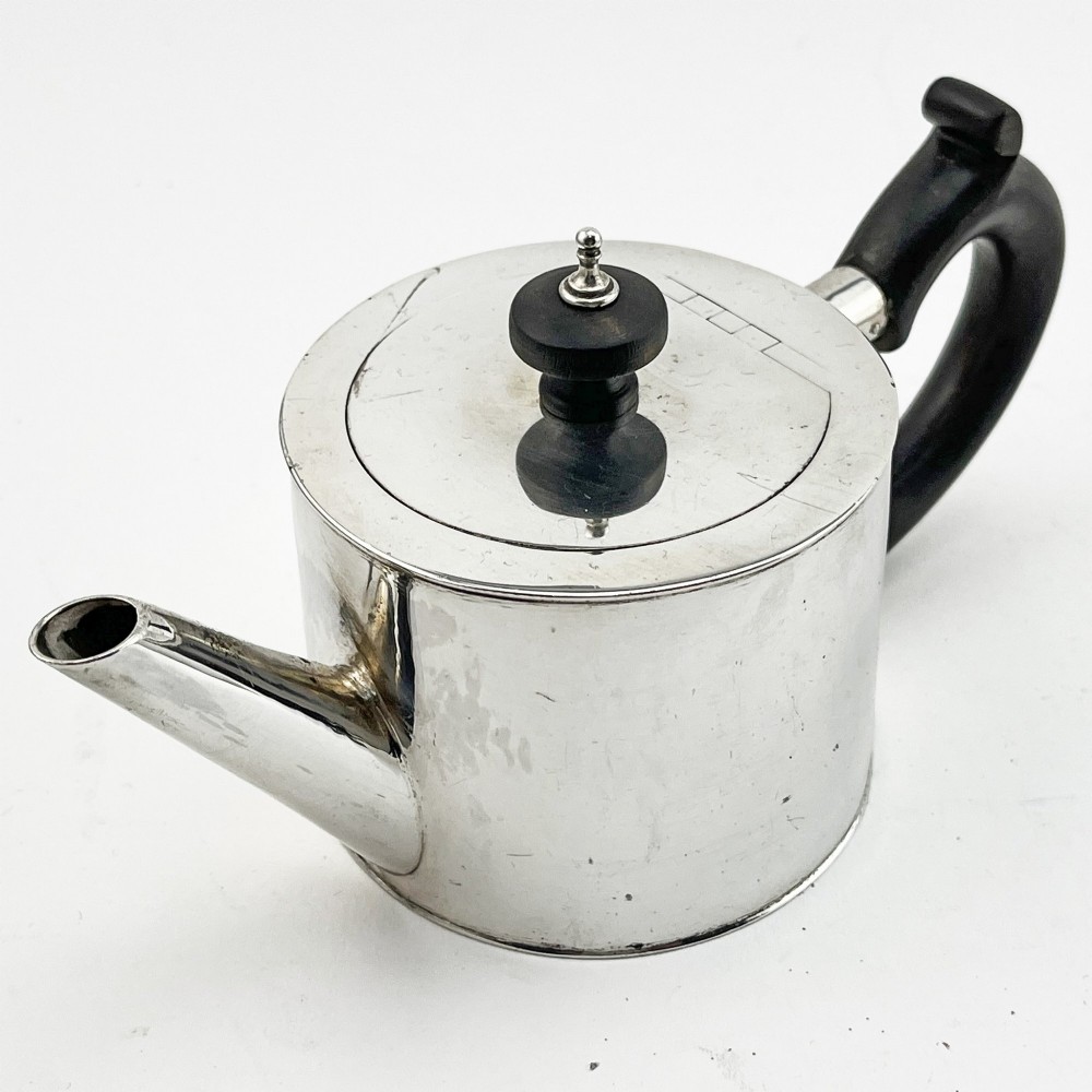 A Georgian sterling silver bachelor teapot featuring a cylindrical drum body, straight spout, and dark wooden handle and finial.