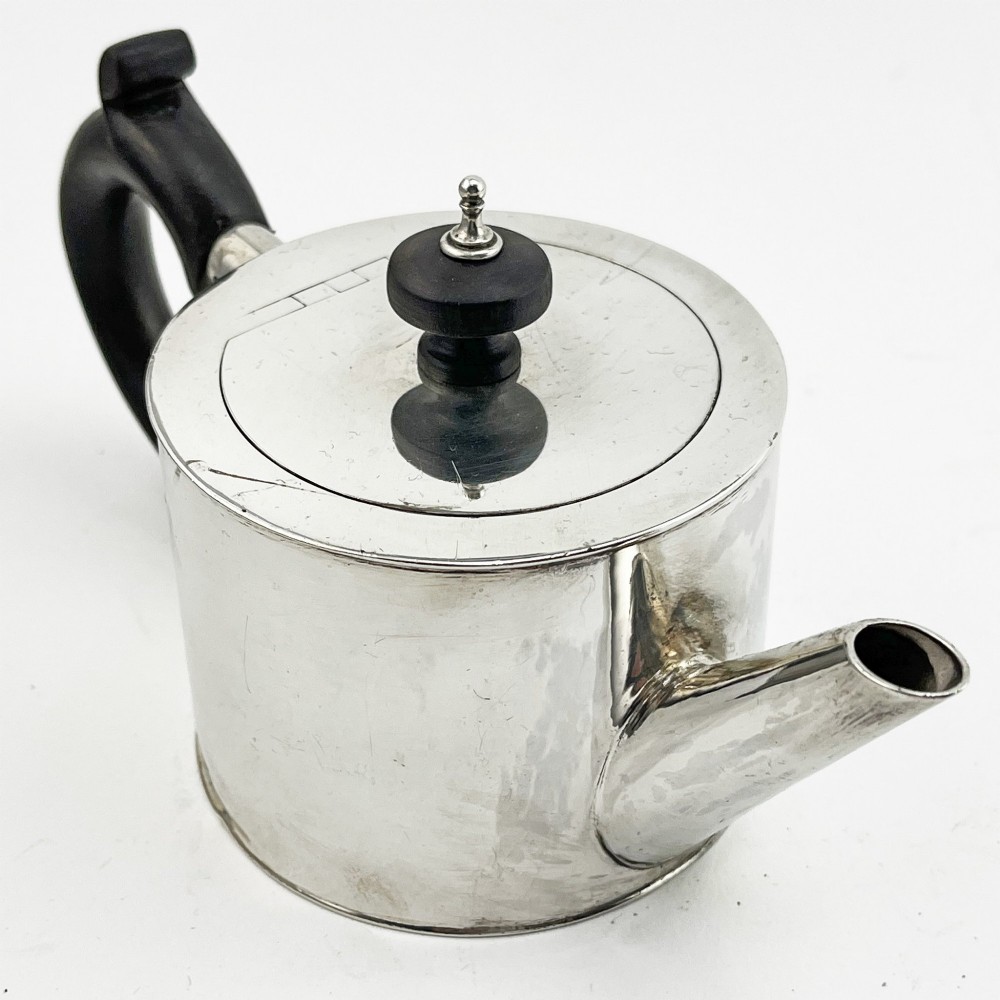 A Georgian sterling silver bachelor teapot featuring a cylindrical drum body, straight spout, and dark wooden handle and finial. View V