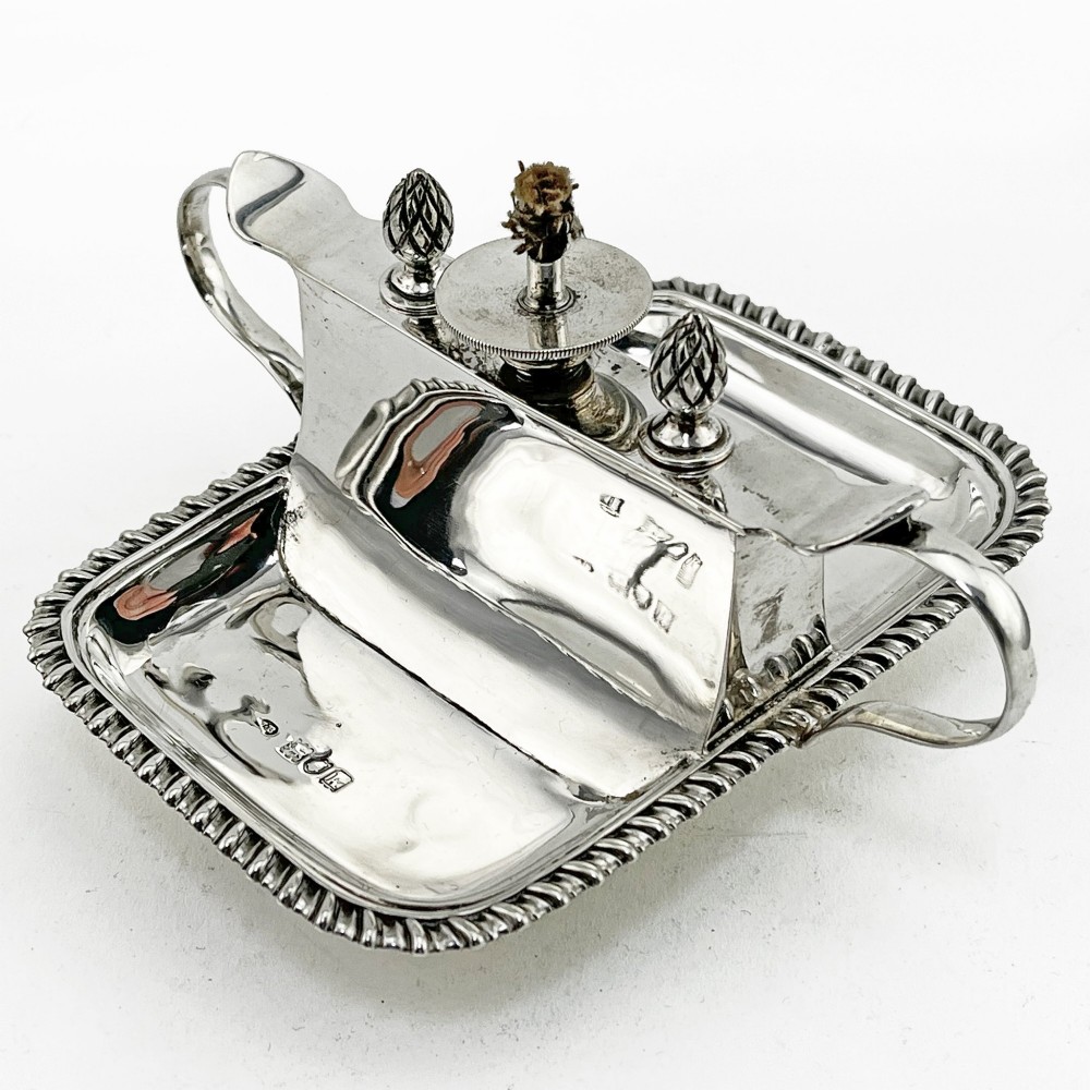 An Edwardian sterling silver table cigar lighter featuring a gadrooned tray border, central wick reservoir, twin handles, and hallmarks.
