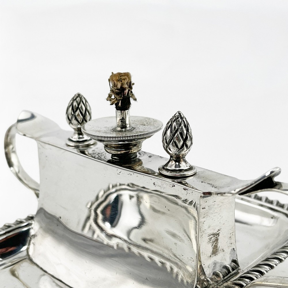 An Edwardian sterling silver table cigar lighter featuring a gadrooned tray border, central wick reservoir, twin handles, and hallmarks. View II