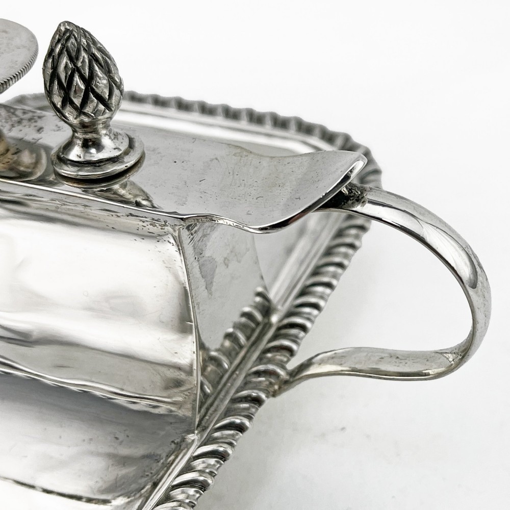 An Edwardian sterling silver table cigar lighter featuring a gadrooned tray border, central wick reservoir, twin handles, and hallmarks. View IV