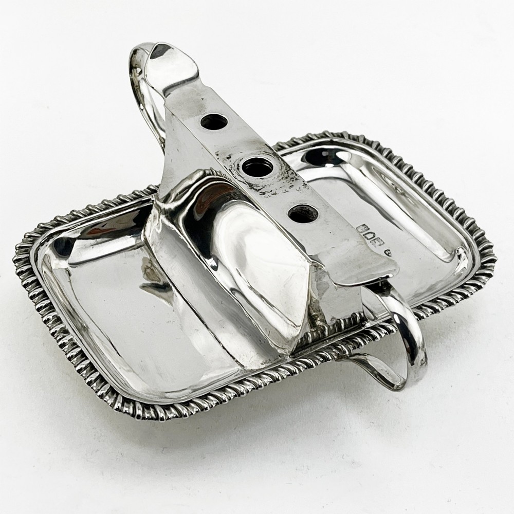 An Edwardian sterling silver table cigar lighter featuring a gadrooned tray border, central wick reservoir, twin handles, and hallmarks. View VI