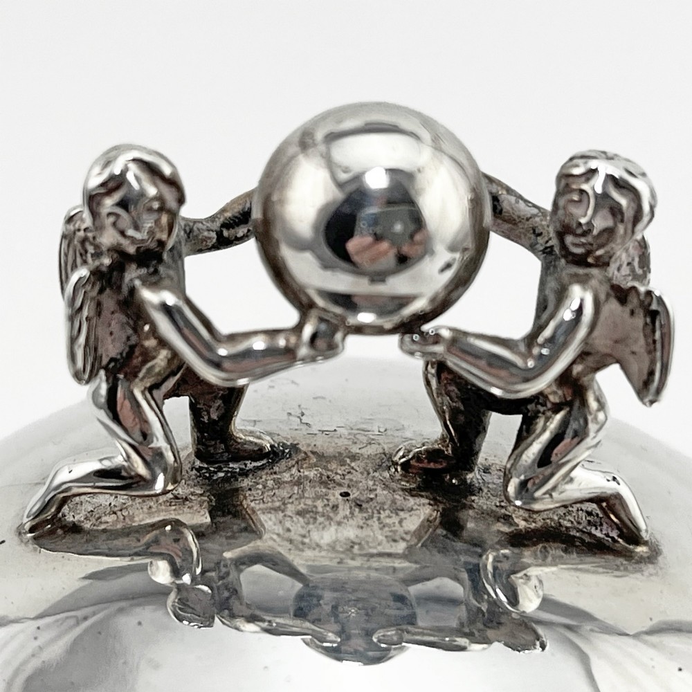 A spherical George III sterling silver soap box featuring engraved scrollwork and a finial shaped like two cherubs holding an orb. View II
