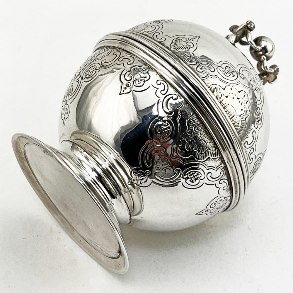 A spherical George III sterling silver soap box featuring engraved scrollwork and a finial shaped like two cherubs holding an orb. View VII