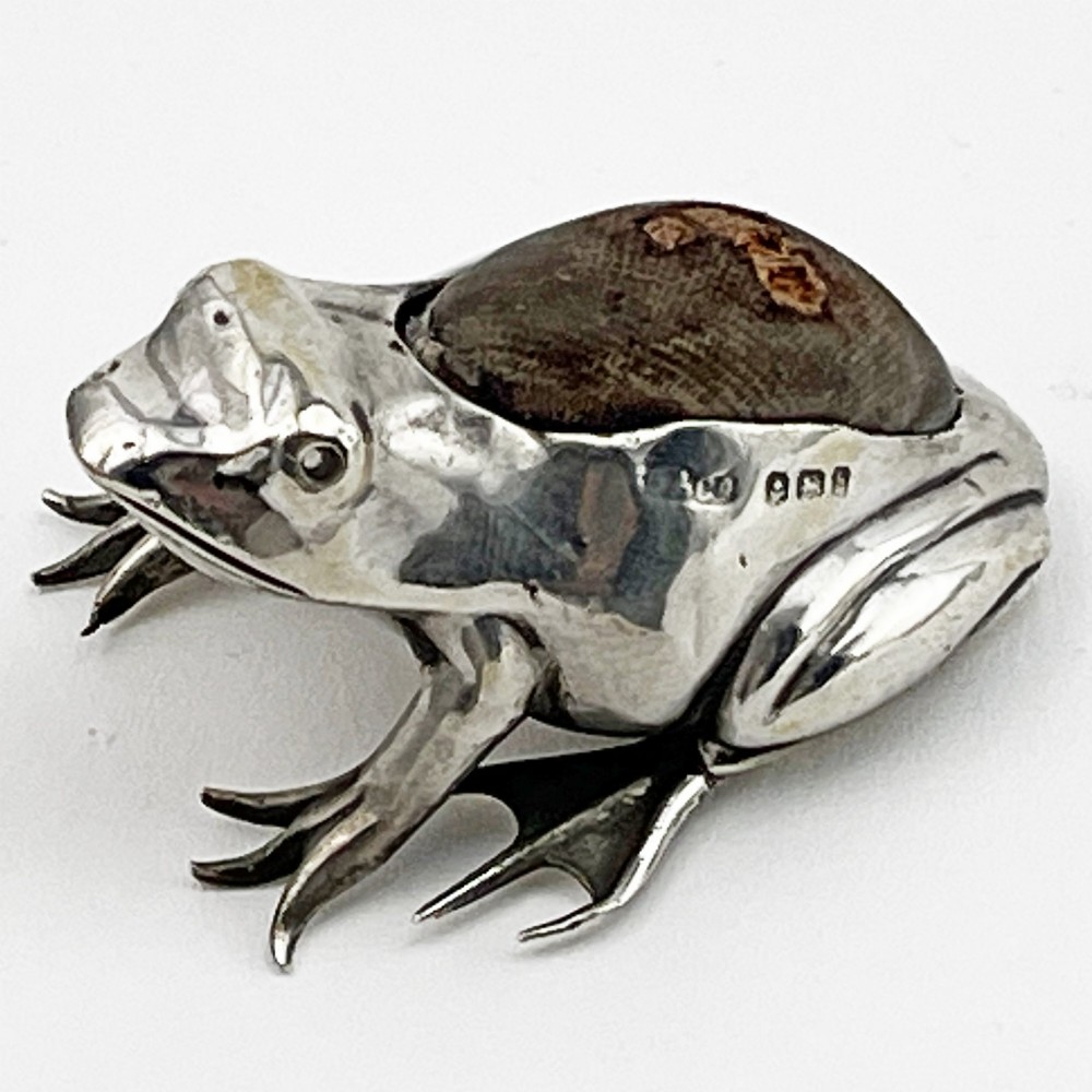 An Edwardian sterling silver pin cushion cast in the realistic shape of a frog with a dark fabric cushion inset on its back.