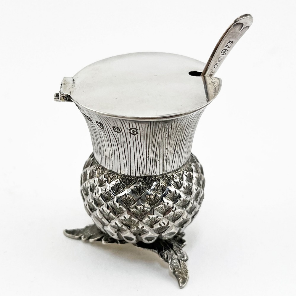 A sterling silver mustard pot styled in the shape of a Scottish thistle with a flat hinged lid and an inserted matching silver spoon. View II