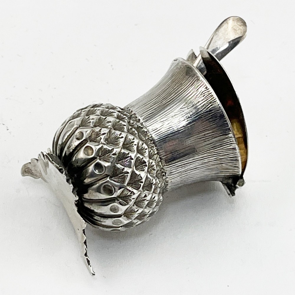 A sterling silver mustard pot styled in the shape of a Scottish thistle with a flat hinged lid and an inserted matching silver spoon. View V