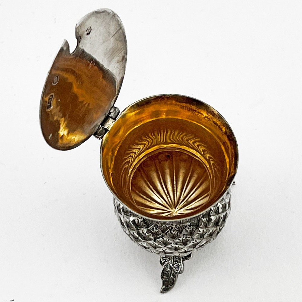 A sterling silver mustard pot styled in the shape of a Scottish thistle with a flat hinged lid and an inserted matching silver spoon. View VI