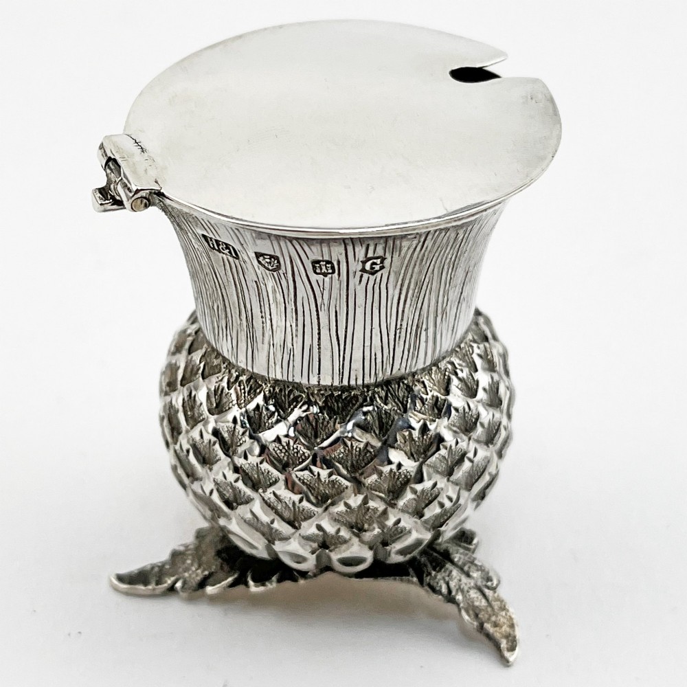 A sterling silver mustard pot styled in the shape of a Scottish thistle with a flat hinged lid and an inserted matching silver spoon. View IX