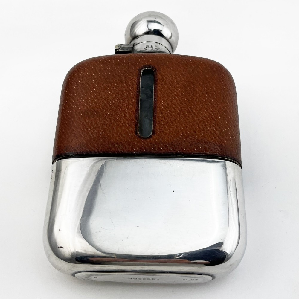 A silver plated hip flask featuring a textured brown leather upper section with a vertical sight window and a polished domed cap. View II