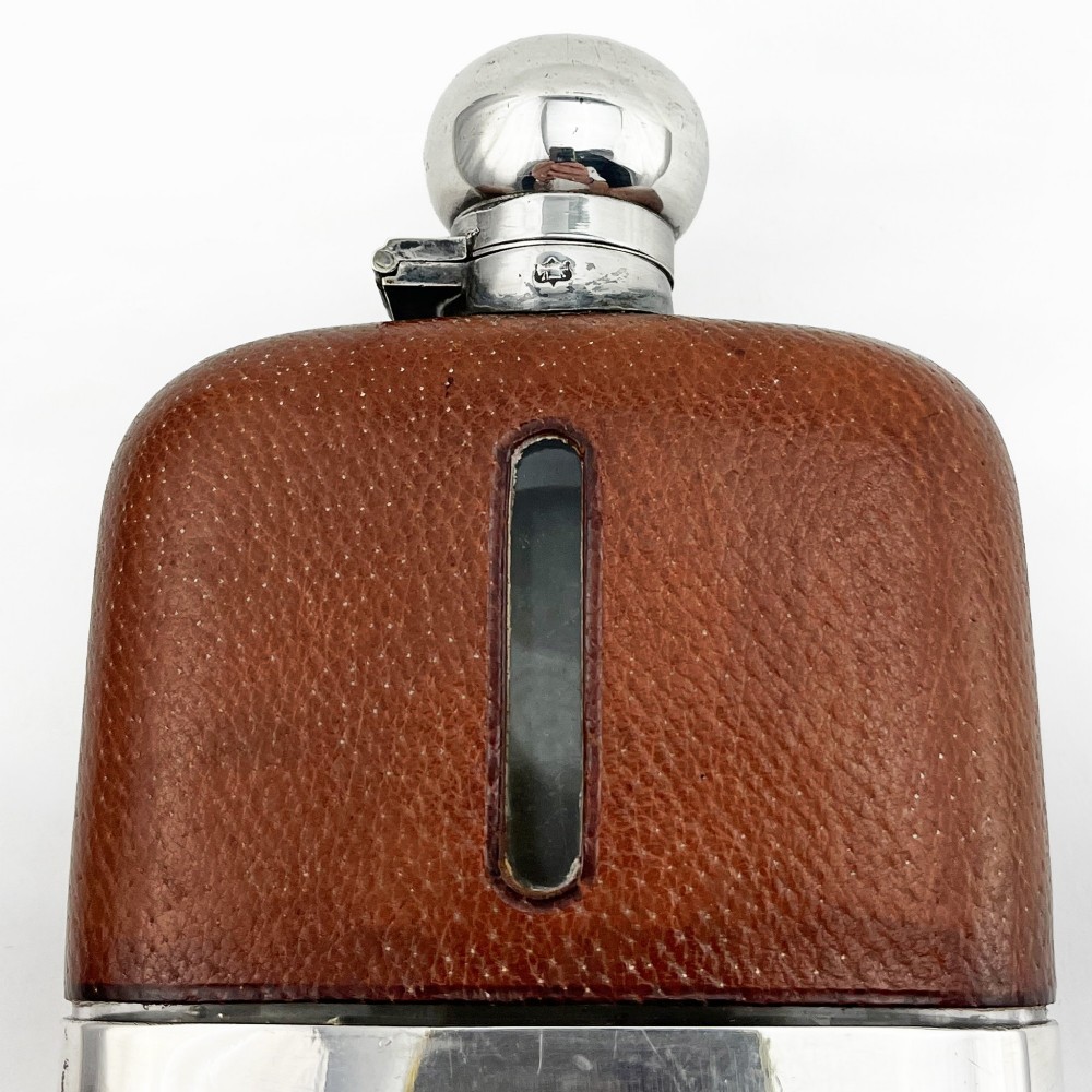 A silver plated hip flask featuring a textured brown leather upper section with a vertical sight window and a polished domed cap. View III