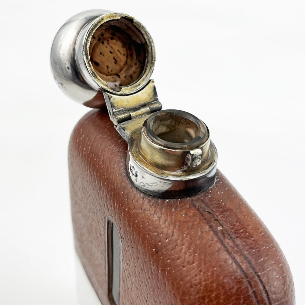 A silver plated hip flask featuring a textured brown leather upper section with a vertical sight window and a polished domed cap. View IV